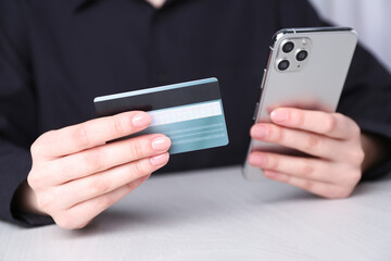 Online payment. Woman with smartphone and credit card at white wooden table, closeup