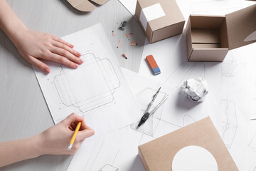 Woman creating packaging design at light wooden table, top view - obrazy, fototapety, plakaty