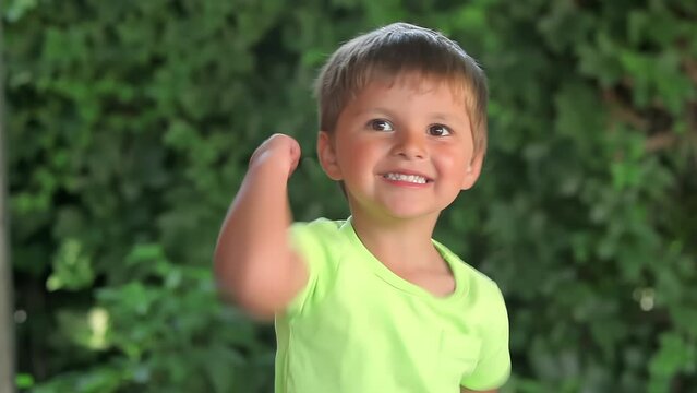 The little cheerful boy in a green t-shirt is showing bicep muscles outdoors. High quality 4k footage