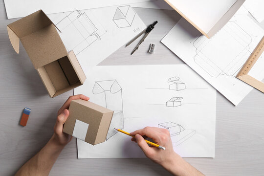 Man creating packaging design at light wooden table, top view