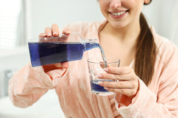 Young woman using mouthwash indoors, closeup view