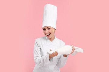 Happy professional confectioner in uniform holding piping bag on pink background
