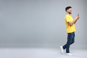 Happy young man using smartphone on grey background, space for text