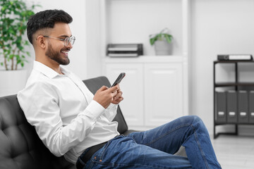 Handsome young man using smartphone on sofa in office