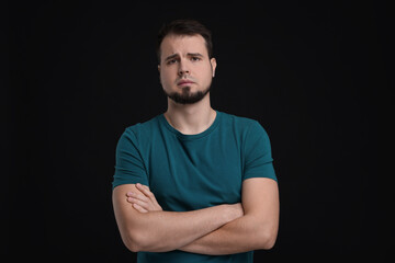 Portrait of sad man with crossed arms on black background