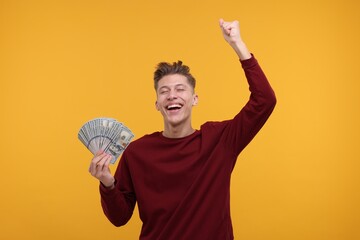 Happy man with dollar banknotes on yellow background