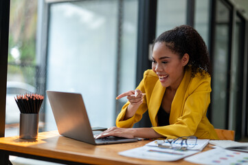 Vibrant businesswoman in a yellow blazer focusing on her laptop screen with excitement in a modern...
