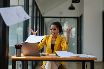 A businesswoman in a yellow jacket expressing frustration and throwing papers into the air at her...