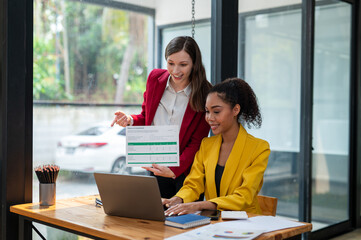 A team of businesswomen engaged in reviewing a financial document on return on investment, discussing strategies over a laptop in the office.