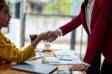 Close-up of two businesswomen shaking hands over a desk, symbolizing a successful agreement or...