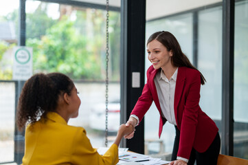 Two professional women in a friendly handshake over an office desk, sealing a business deal with positive demeanor and smiles.