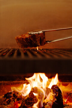 A thick piece of meat sizzles on a grill over flames vertical