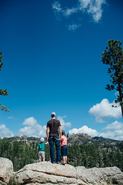 Dad and two sons stand on rocks overlooking mountains and sky