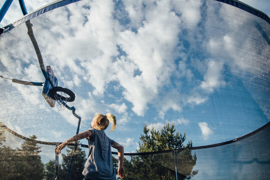 Girl playing basketball on trampoline with wide view of clouds in sky
