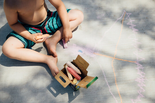 Overhead view of young boy drawing with chalk on sidewalk in summer