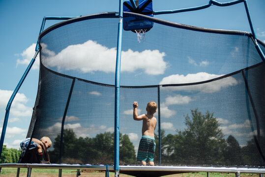 Wide view of two boys jumping on trampoline outdoors with clouds