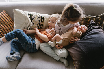 a growing family of siblings snuggling on the couch with newborn