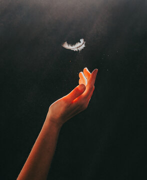 Illuminated feather falling into outstretched hand in the dark..