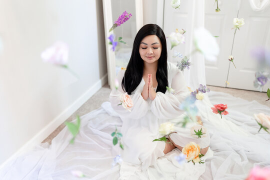 Zen asian woman meditating, praying, hanging flowers, bright whi