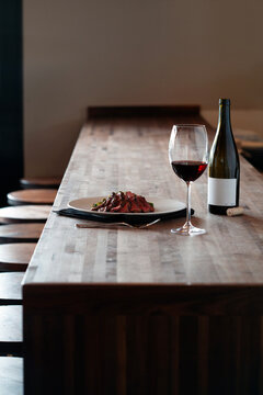 A plated meat entree served with a glass of red wine on a bar table
