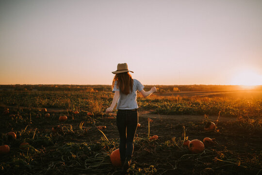 Young redhead woman in a hat runs in a pumpkin patch at sunset