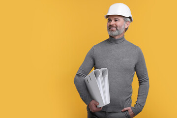 Architect in hard hat holding folders on orange background. Space for text - obrazy, fototapety, plakaty