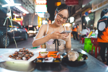 Asian foodie tourist woman eating raw oyster seafood at China town asia street food night market