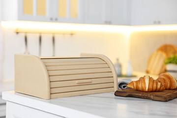 Wooden bread box and board with croissants on white marble table in kitchen