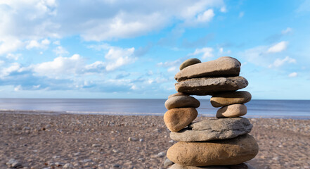 Stack of zen stones with by the sea blurry blue sky backgroud, Close up Balancing of pebble rocks stacked on top of each other on the sand beach.Zen like concepts