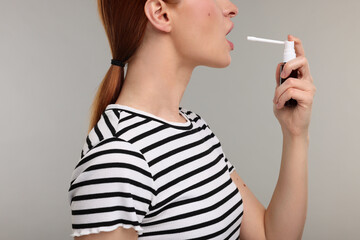 Young woman using throat spray on grey background, closeup