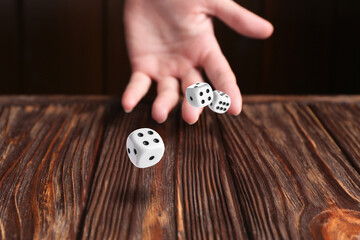 Woman throwing white dice on wooden table, closeup