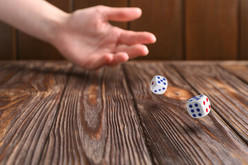 Woman throwing white dice on wooden table, closeup