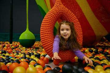 Smiling baby girl swinging on hanging ball playing in balls pool - 780341252
