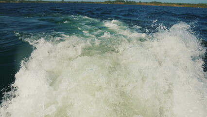 A trail of water on a lake seen behind a speeding motorboat on a clear day, the surface of the water