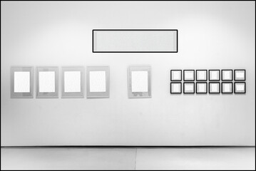 In sala di esposizione dalle pareti bianche sono esposte cornici con l'interno vuoto. L'interno bianco delle cornici permette l'inserimento di immagini o testo. Serie di cornici allineate.