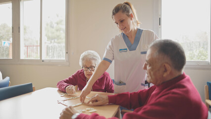 Nurse with seniors playing dominoes at care home