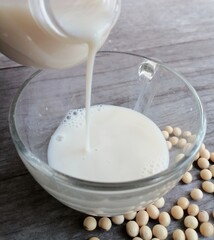 Pouring soy milk with soybean on wood background