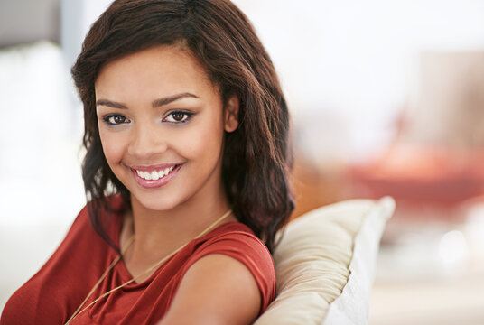 Woman, smile and relax on sofa for portrait in living room on holiday with confidence, pride and break on weekend. Girl, happy and sitting on couch in lounge for break at apartment in Colombia