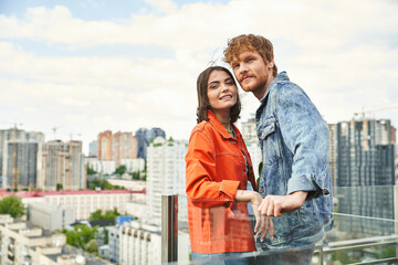 A man and a woman stand side by side on a balcony overlooking the city skyline