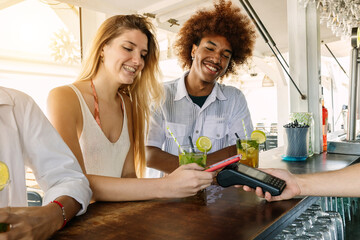 Young couple using contactless credit or debit card for payment at beach bar