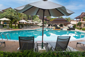 Beautiful swimming pool in tropical resort with palms chairs loungers under umbrella . Luxury travel vacation