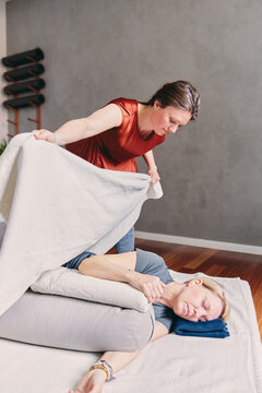 Therapist using a blanket during a massage. The female client lies comfortably on her side, with her eyes closed, while the therapist carefully places a blanket over her