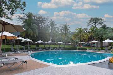 Beautiful swimming pool in tropical resort with palms chairs loungers under umbrella . Luxury...