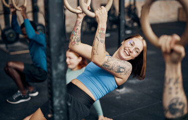 A fit woman with tattoos, smiles at her diverse friends during a gym workout class with rings