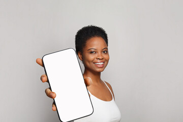 Young healthy woman holding smartphone with white empty blank screen display on gray studio wall...