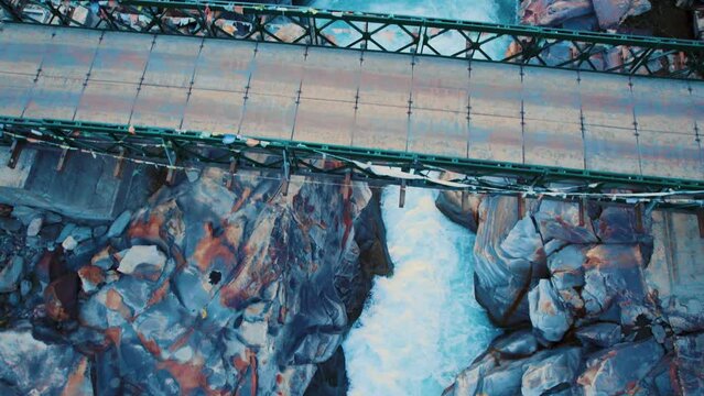 4K aerial shot of Bhaga river flowing between rocky canyon and wooden bridge passing above river stream. Aerial View of River in Lahaul, Himachal Pradesh, India. Old epic wooden bridge over blue river