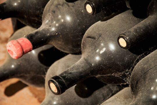 Vintage dusty wine bottles aged to perfection in a rustic cellar, evoking traditions of winemaking