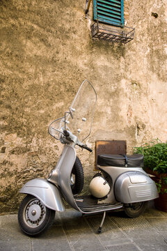 A vintage scooter stands parked by a weathered wall, its classic design and accompanying helmet painting a picture of timeless adventure in a serene alleyway