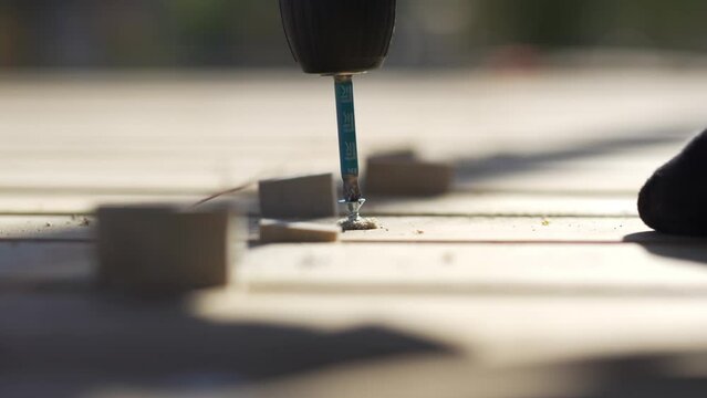 Fastener-driving machine swiftly turns coach bolt into wooden surface closeup. Daily activities proceed as usual at urban building site