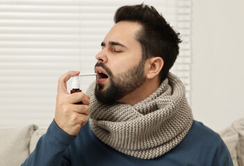 Young man with scarf using throat spray indoors